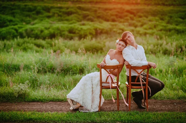 Красивая молодая невеста и жених сидят стулья в свете заката — стоковое фото