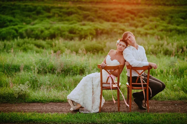 Belle jeune mariée et marié chaises assises dans la lumière du coucher du soleil — Photo