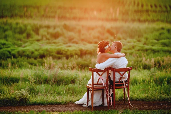 Belle jeune mariée et marié chaises assises dans la lumière du coucher du soleil — Photo