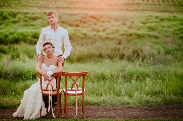Bela noiva e noivo sentado cadeiras na luz do pôr do sol — Fotografia de Stock