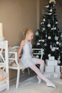 Little ballet dancer sitting white bathing suit near a Christmas tree