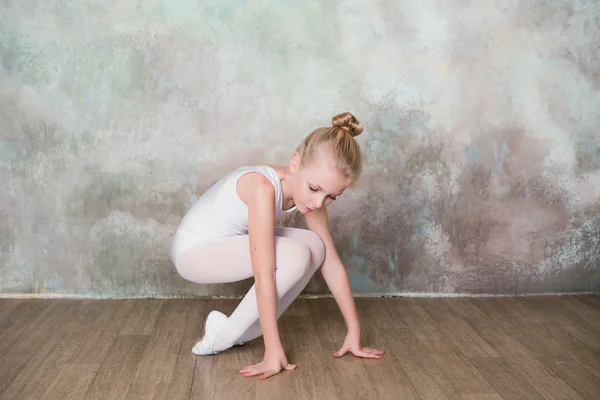 Little ballet dancer doing stretching before class in a white bathing suit — Stock Photo, Image