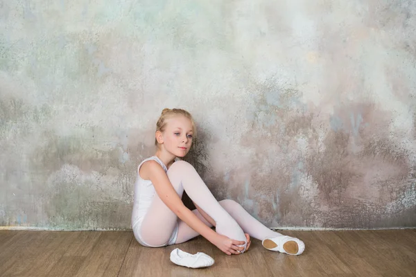 Little ballet dancer doing stretching before class in a white bathing suit — Stock Photo, Image