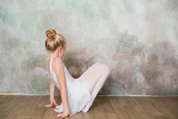 Little ballet dancer doing stretching before class in a white bathing suit — Stock Photo, Image