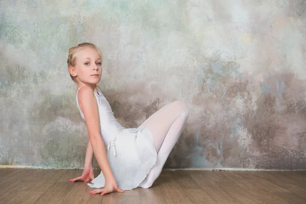 Little ballet dancer doing stretching before class in a white bathing suit — Stock Photo, Image