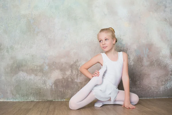 Little ballet dancer doing stretching before class in a white bathing suit — Stock Photo, Image