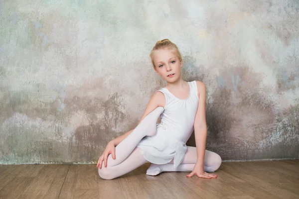 Little ballet dancer doing stretching before class in a white bathing suit — Stock Photo, Image