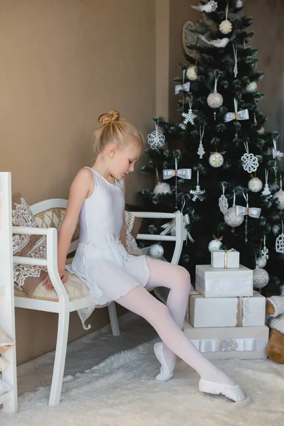 Little ballet dancer sitting white bathing suit near a Christmas tree