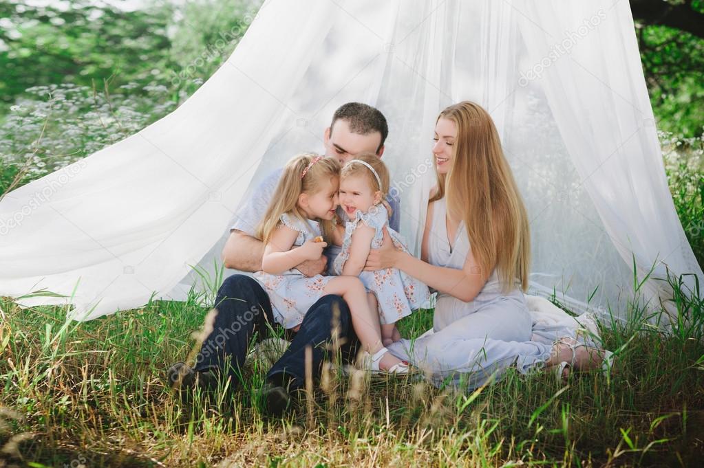 Mom and dad playing on the nature and hugging two daughters