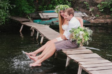 Genç bir çift ile bir tahta köprüden gülüyor üzerinde bir buket çelenk içinde