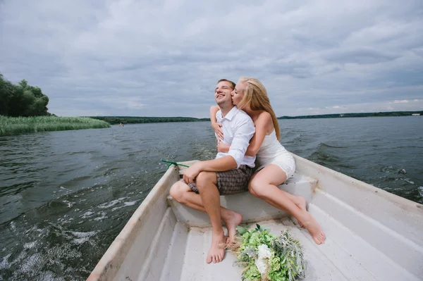 Glada unga par med en bukett och en krans kram sitter i en båt på sjön — Stockfoto