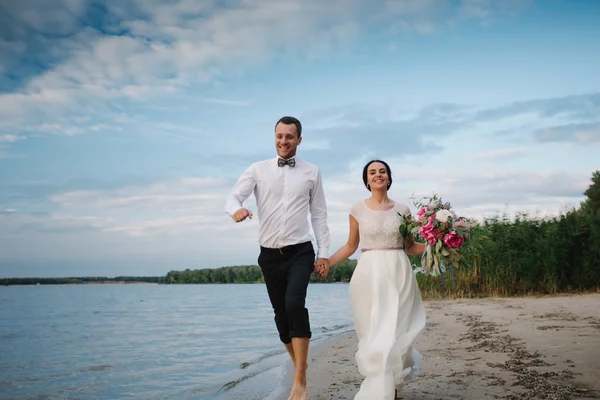 Bruden och brudgummen körs på stranden — Stockfoto