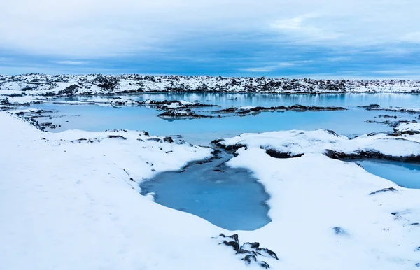Snötäckta lavastenar nära blå lagunen — Stockfoto