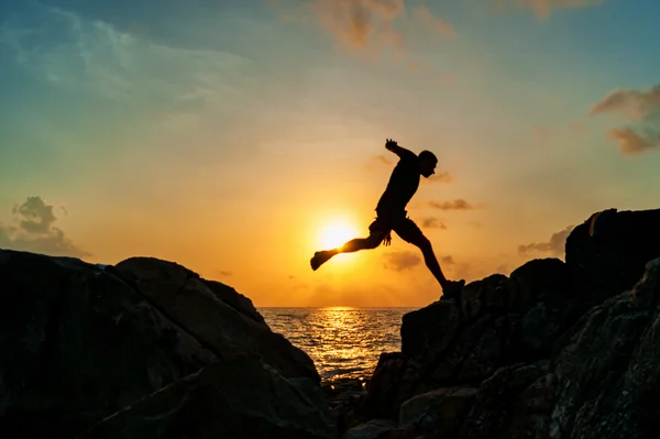 Силуэт человека, бегущего по скалам у моря — стоковое фото