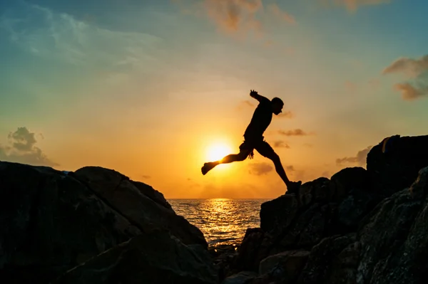 Silueta de un hombre corriendo sobre las rocas junto al mar — Foto de Stock