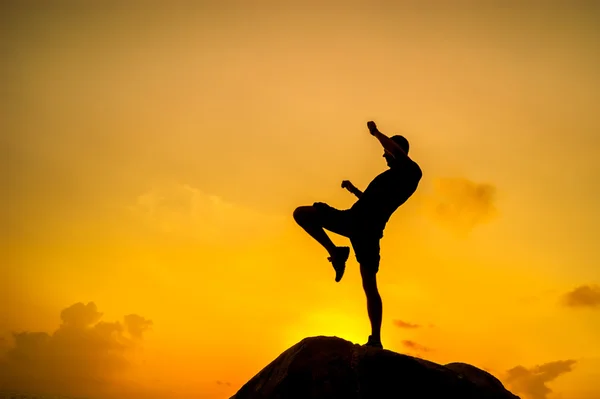 Silueta de un hombre haciendo ejercicios sobre rocas junto al mar al amanecer — Foto de Stock