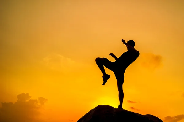 Silueta de un hombre haciendo ejercicios sobre rocas junto al mar al amanecer — Foto de Stock