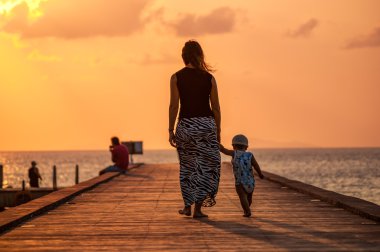 Anne ve çocuğun gün batımında iskelede yürüdükleri arka plan.