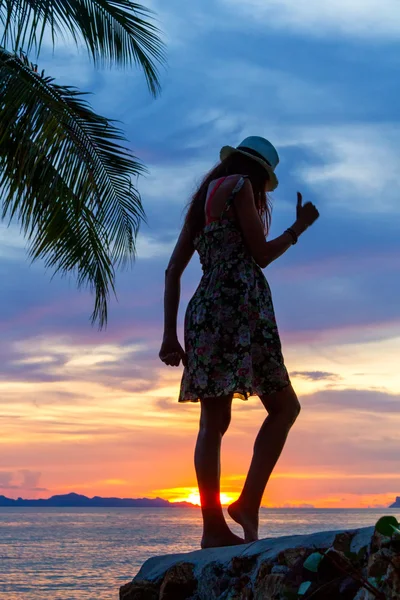 Silhueta de uma menina dançante em uma rocha junto ao mar em um fundo de pôr do sol tropical — Fotografia de Stock