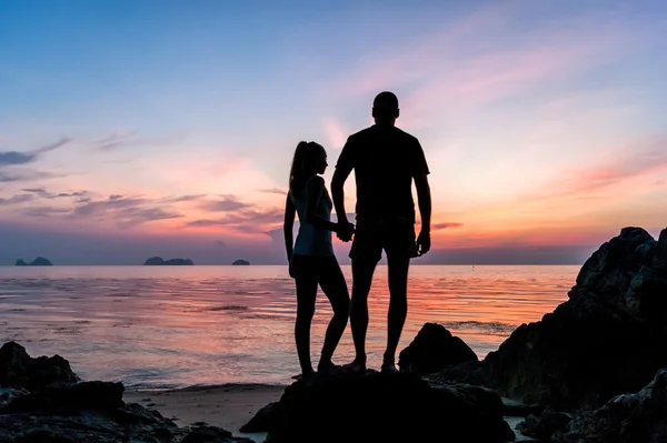 シルエット若いカップルで手をつないでと熱帯の夕日の浜に立って — ストック写真