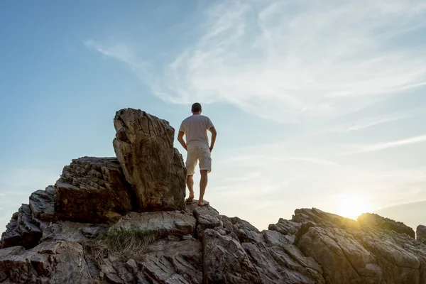 O homem está em cima de uma pedra a ver o pôr do sol tropical — Fotografia de Stock