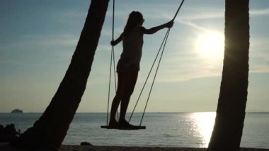 Denize karşı tropik sahilde bir salıncak üzerinde genç kadın