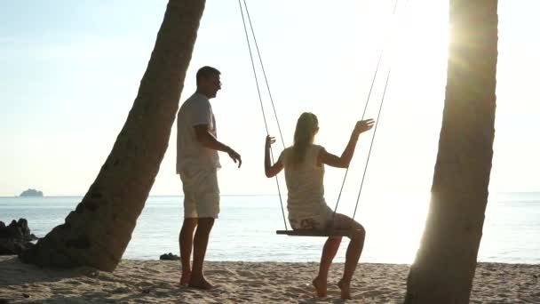 Pareja joven en un columpio en la playa tropical contra el mar — Vídeo de stock