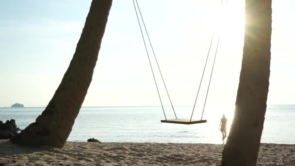 夕日を背景にスイングにビーチを歩いている若いカップル — ストック動画
