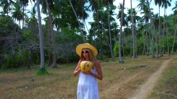 Jonge Kaukasische vrouw met kokos in handen lopen door de jungle — Stockvideo