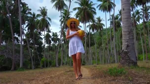 Молодая белая женщина с кокосом в руках, идущая по джунглям — стоковое видео