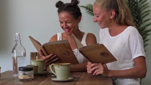 Two young women choose food on the menu and talking in a cafe — Stock Video