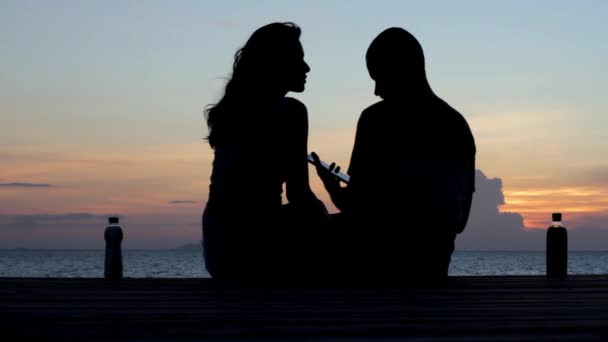 Jeune couple assis sur la jetée au coucher du soleil — Video