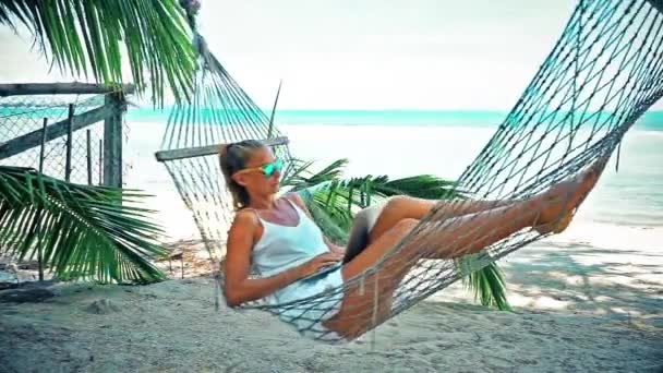 Молодая женщина с ноутбуком в гамаке на пляже — стоковое видео