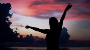 Genç kadın sahilde günbatımı arka plan üzerinde dans