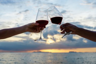 Günbatımı arka planında şarap kadehlerini tokuşturan arkadaşlara yakın.