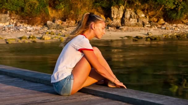 Молода жінка чіпляється за пірс біля моря на фоні заходу сонця — стокове відео