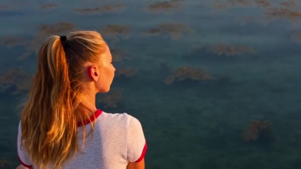 Молодая женщина, стоящая на пирсе у моря на фоне заката — стоковое видео