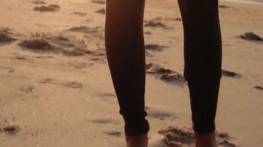 Genç bir kadın rengarenk günbatımı arka planında sahilde koşmaya hazırlanıyor.