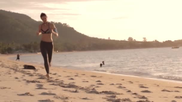 カラフルなサンセットを背景にビーチを走っている若い女性が — ストック動画