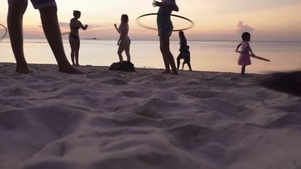 日落时带着呼啦圈在海滩上跳舞的少女的侧影 人们在海滩上散步 欣赏着五彩缤纷的日落 — 图库视频影像