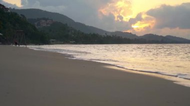 Tropikal kumlu sahilde gün batımında deniz sörfü. Yavaş çekim videosu