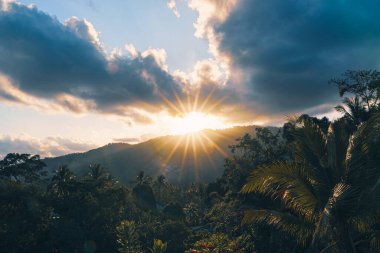 Dağda ve vadide, sonbahar günbatımında evleri ve ormanları olan dramatik bulutların arasından parlayan muhteşem güneş ışınları.