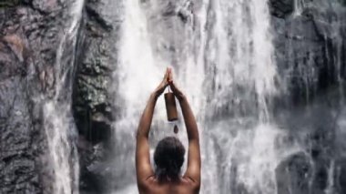Şelalenin yanında duran kadın meditasyon yapıyor.