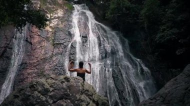 Şelalenin yanında duran kadın meditasyon yapıyor.