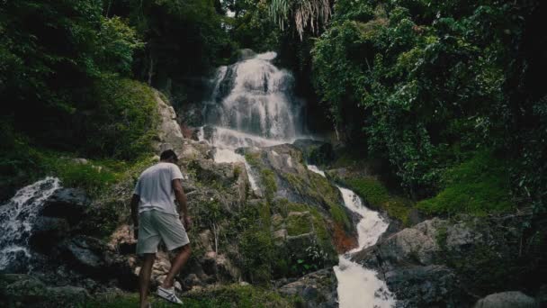 Jovem Roupas Brancas Casuais Sobe Rochas Olha Para Uma Cachoeira — Vídeo de Stock