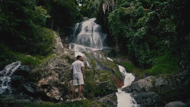 Seorang Pemuda Berpakaian Putih Santai Memanjat Batu Dan Melihat Air — Stok Video