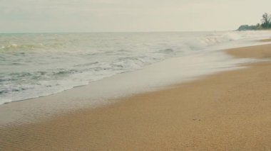 Gün batımında kumlu bir kumsalda sörf ve dalgalarla dolu bir sahil şeridi.
