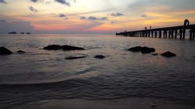 Renkli gün batımı, insanlar iskelede duruyor.