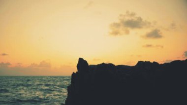 Gün doğumunda deniz kenarındaki kayalıklarda duran bir adamın silueti.