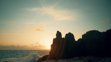 Gün doğumunda deniz kenarındaki kayalıklarda duran bir adamın silueti.